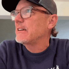 a man wearing glasses and a hat with the letter k on the front of his shirt
