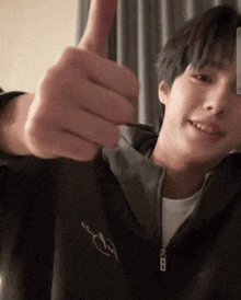 a young man wearing a black jacket is giving a thumbs up sign .