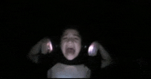 a young boy is screaming in the dark with a flashlight behind him .