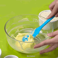 a person is mixing butter in a glass bowl with a blue spatula and the words mr.cakes on the bottom right