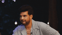 a man with a beard wearing a pearl necklace looks at the camera