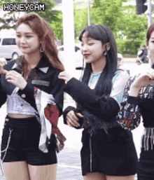 three young women are standing next to each other on a sidewalk .