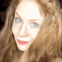 a woman with red hair and blue eyes is smiling for the camera .