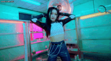 a woman in a crop top and leather pants is dancing in a room with a magnifying glass in the background