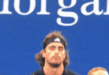 a man wearing an adidas headband stands in front of a blue background that says morgan