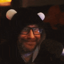 a man wearing glasses and a black hat with white ears is giving an ok sign