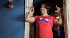 a man in a red shirt is standing in a doorway and waving .