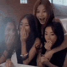 a group of young women are laughing together and covering their mouths