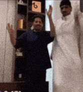 two men are standing next to each other in front of a bookshelf .