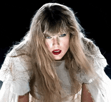 a woman with long blonde hair and red lipstick is wearing a white cape