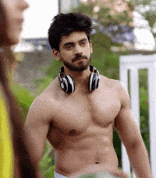 a shirtless man with headphones around his neck looks at a woman