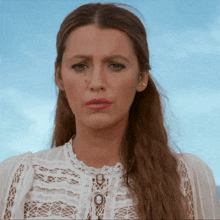 a woman wearing a white lace top looks at the camera with a blue sky in the background