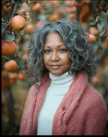 a woman with gray hair is wearing a pink sweater and white turtleneck
