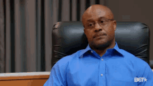 a man in a blue shirt is sitting in a chair with bet on his shirt