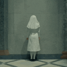 a nun in a white uniform stands in front of a gray wall
