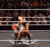 two women are wrestling in a wrestling ring with a crowd watching .