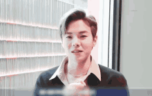 a young man wearing a black shirt and a necklace is looking at the camera