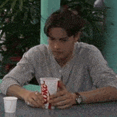 a man is sitting at a table holding a coke cup