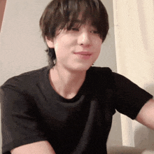 a young man wearing a black t-shirt is smiling while sitting on a couch .