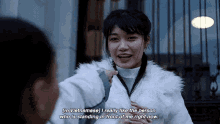 a woman in a white fur coat is talking to a man in front of a fence .