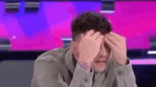 a man is covering his face with his hands in front of a purple background .