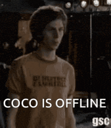 a man wearing a t-shirt that says `` coco is offline '' is standing in front of a stage .