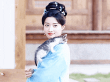 a woman in a blue dress is holding a small cat