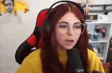 a girl with red hair and glasses is wearing headphones and a yellow sweater while sitting in front of a microphone .