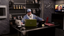 a man sitting at a desk with two laptops and a sign that says coca cola on the wall