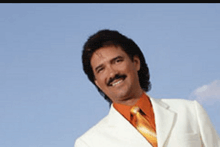 a man in a white suit and orange tie smiles for the camera