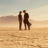 a man and a woman standing in the middle of a desert