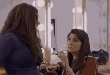 two women are standing next to each other in a dressing room applying makeup .