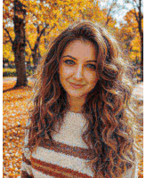 a woman with long curly hair wearing a striped sweater is standing in a park with autumn leaves .