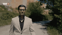 a man in a suit and glasses stands in front of a sign that says trt1 on it