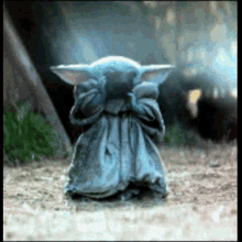 a baby yoda from star wars is covering his eyes with his hands while standing on the ground .
