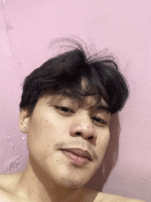 a young man without a shirt is looking at the camera with a pink wall behind him