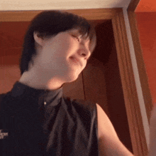 a man wearing a black sleeveless shirt is standing in front of a door and smiling .