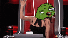 a woman sitting in a chair with a green face on her head and the words #thevoice nbc on the bottom