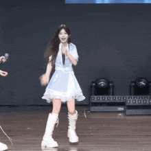a girl in a blue dress and white boots is singing into a microphone on stage