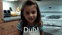 a little girl is sitting in front of a stove with the words duh on her face