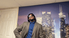 a man wearing sunglasses and a suit stands in front of a city skyline