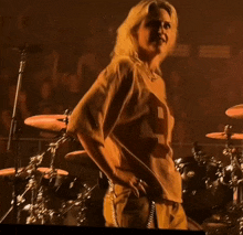 a woman stands on a stage with her hands on her hips and a drum set in the background