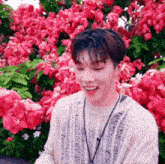 a young man is standing in front of a bush of pink flowers and smiling .