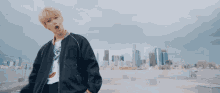 a young man in a black jacket is standing on a rooftop in front of a city skyline