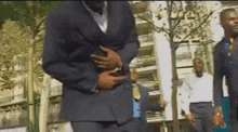 a man in a suit and tie is standing in front of a building holding his stomach .