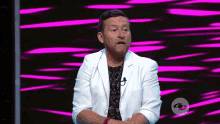 a man in a white jacket stands in front of a pink and black background
