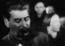 a black and white photo of a man with a mustache talking to a crowd of people .
