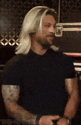 a man with long blonde hair is wearing a black shirt and a watch