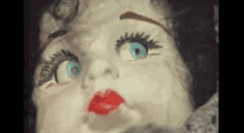 a doll with blue eyes and red lips is looking at the camera .