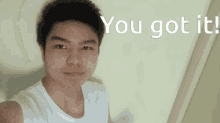a young man in a white tank top is standing in front of a wall that says you got it